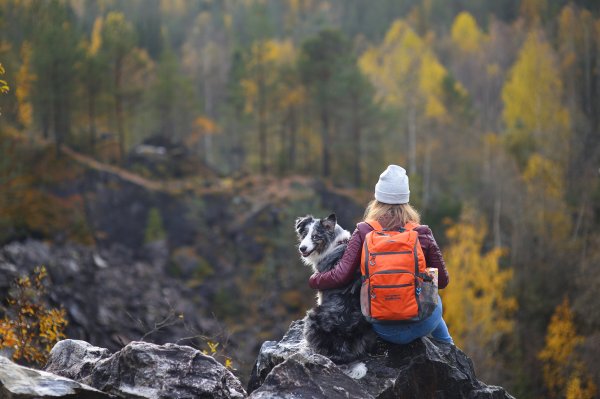 A woman and dog sit on a rocky outcropping with the dog turned towards the camera smiling.