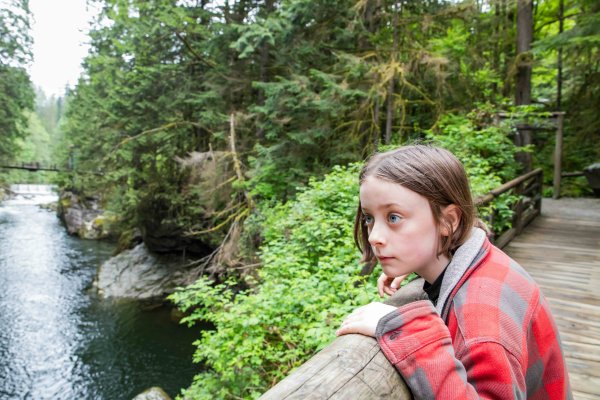 A young person peers out from a bridge, looking at a river and forest.