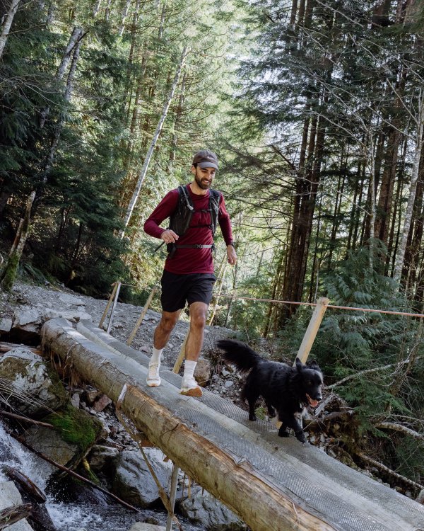 A person runs with their dog across a log bridge.